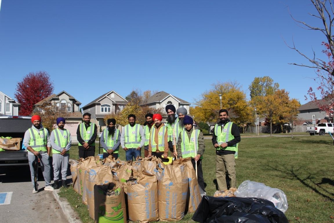 Volunteers standing behind rows of filled paper yard-waste bags collected during the park clean-up