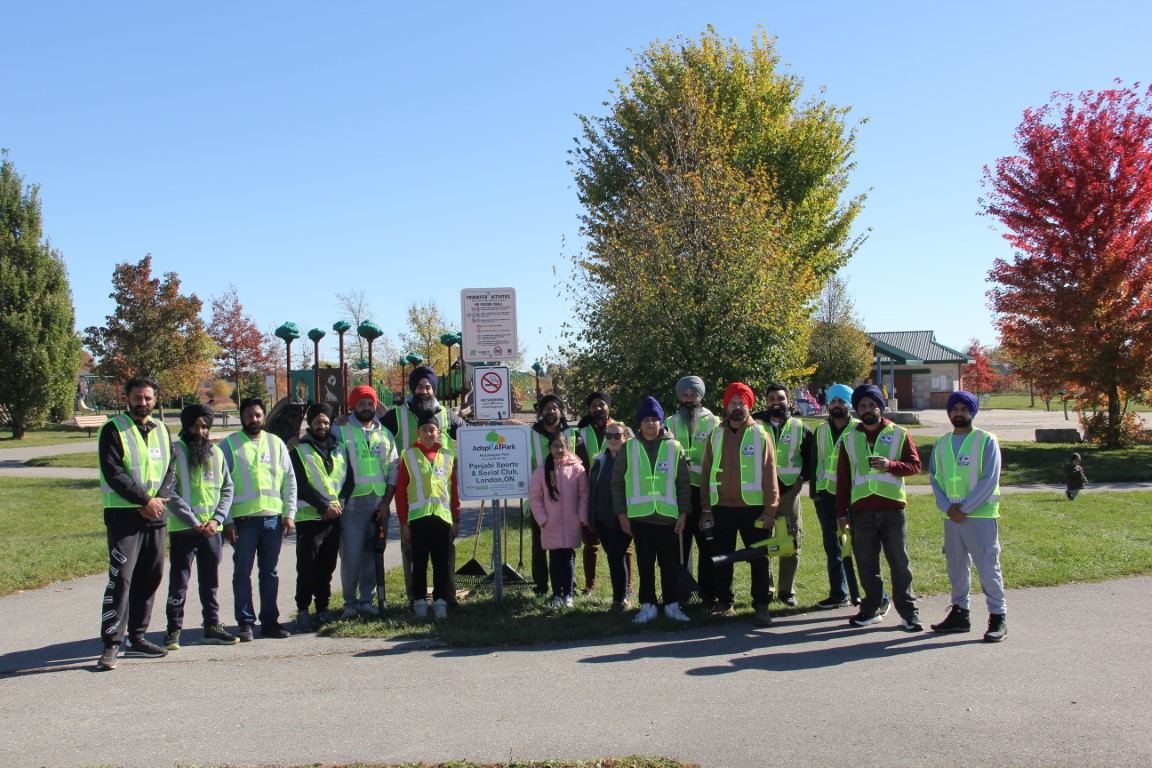 Club volunteers of all ages in high-visibility vests gathered around the Adopt-a-Park sign at Meadowgate Park